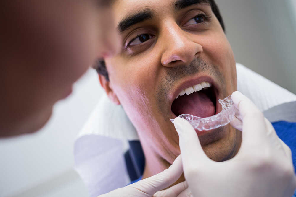 ortodonta zakłada nakładki Invisalign pacjentowi na zęby